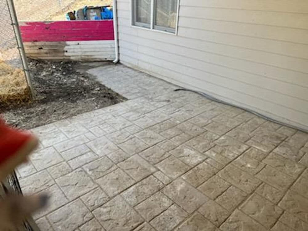Newly installed stamped concrete patio beside a house with a visible fence in the background.