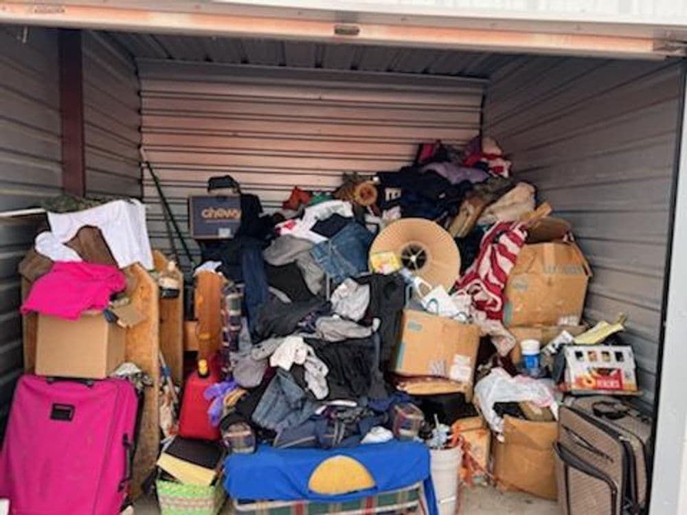 Cluttered storage unit filled with bags, clothes, boxes, and various items.
