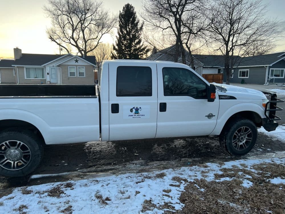 White Ford F-250 truck parked on a snowy driveway, featuring a logo on the door.