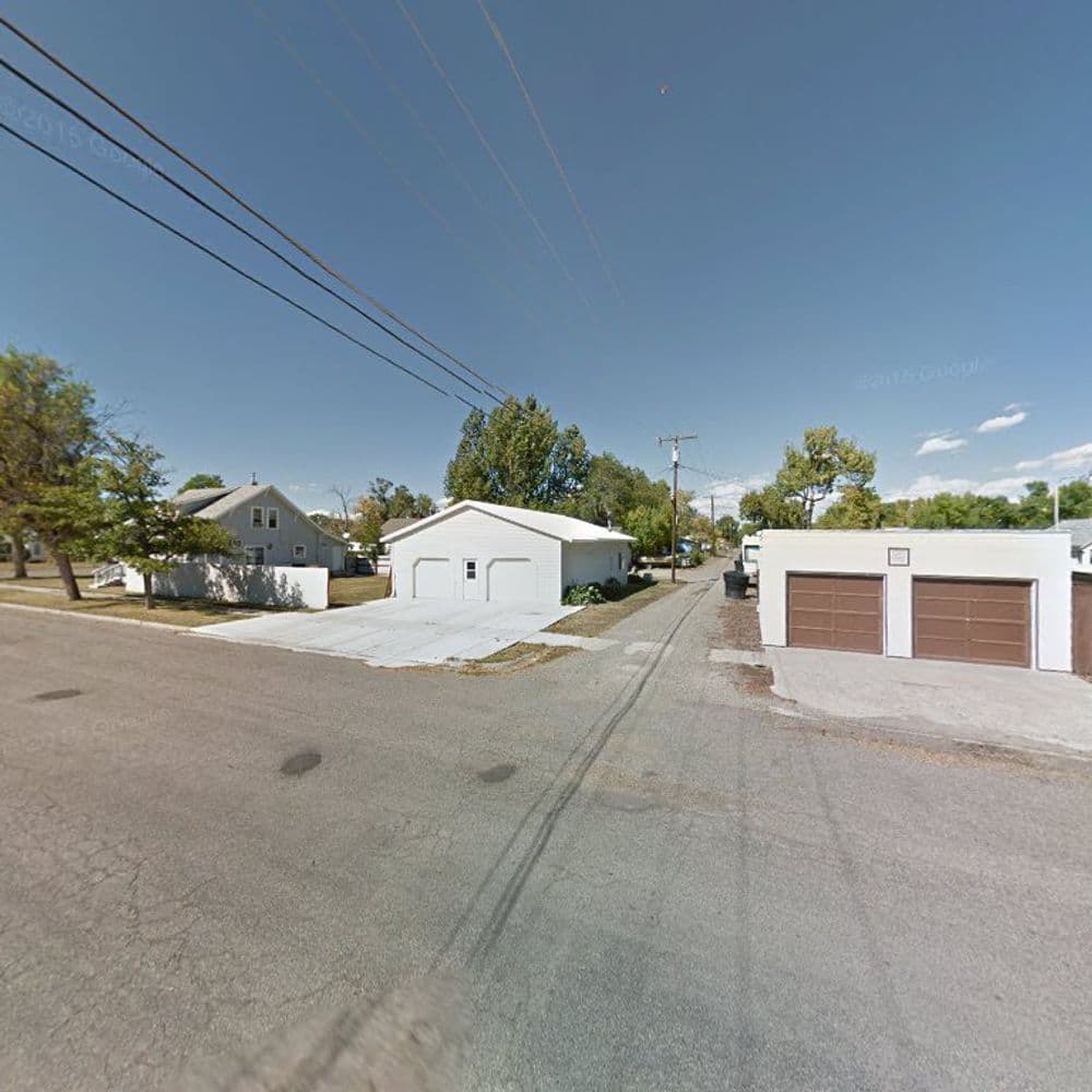 White buildings and garages along a quiet street with power lines under a blue sky.