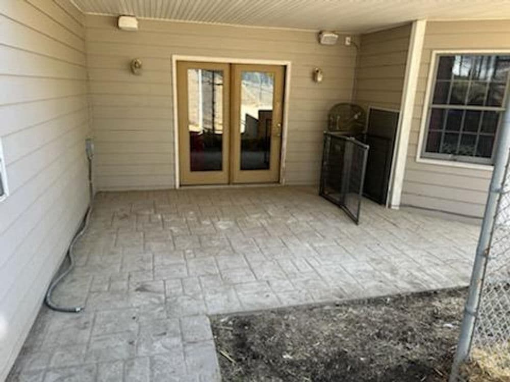 Covered patio with double doors, decorative stone flooring, and a fenced area.