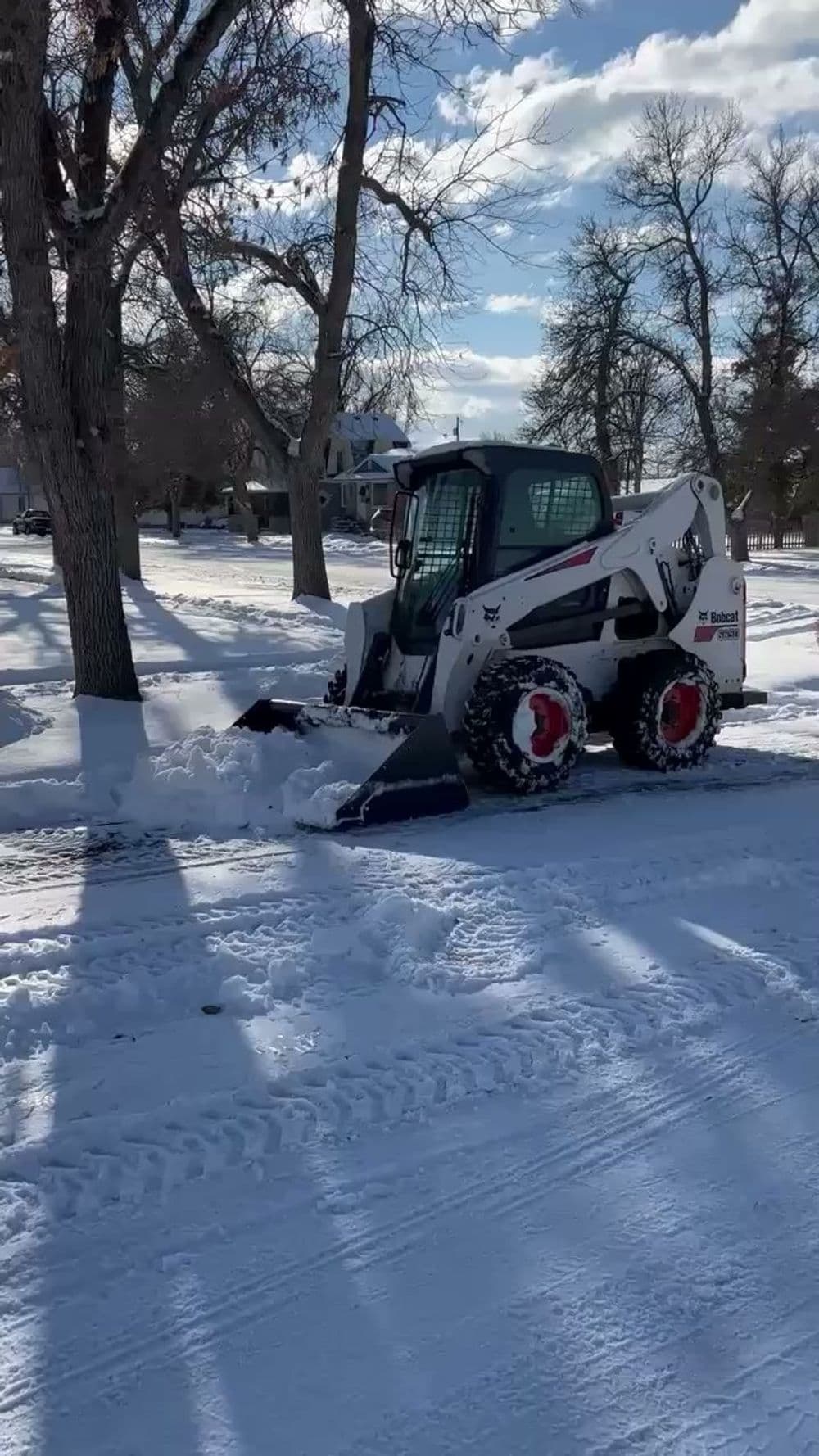 Snow plow clearing a residential street covered in snow, with trees in the background.