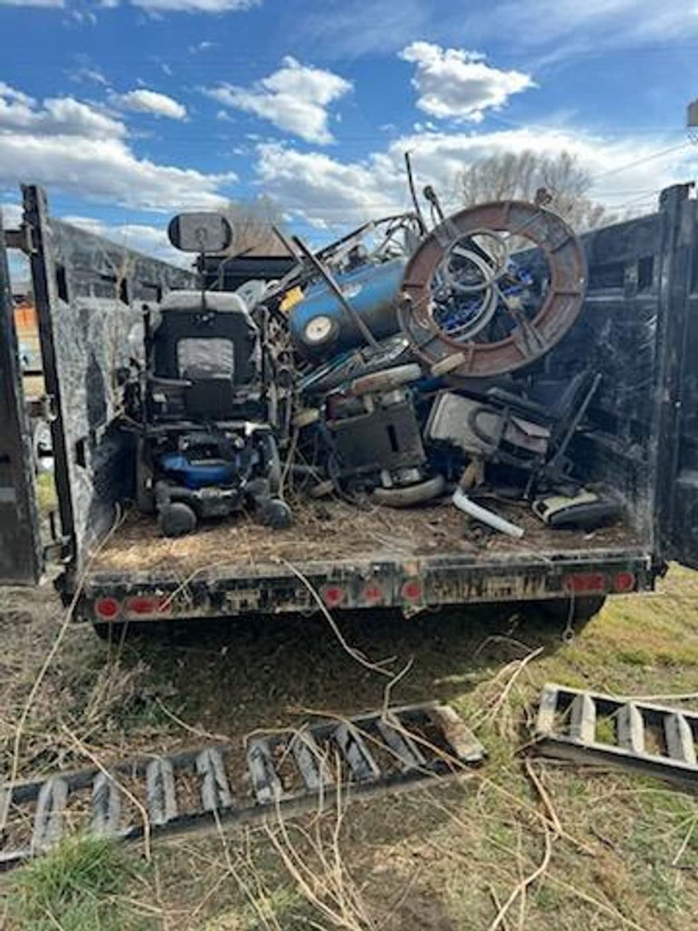 Dump truck filled with discarded furniture and equipment under a blue sky.
