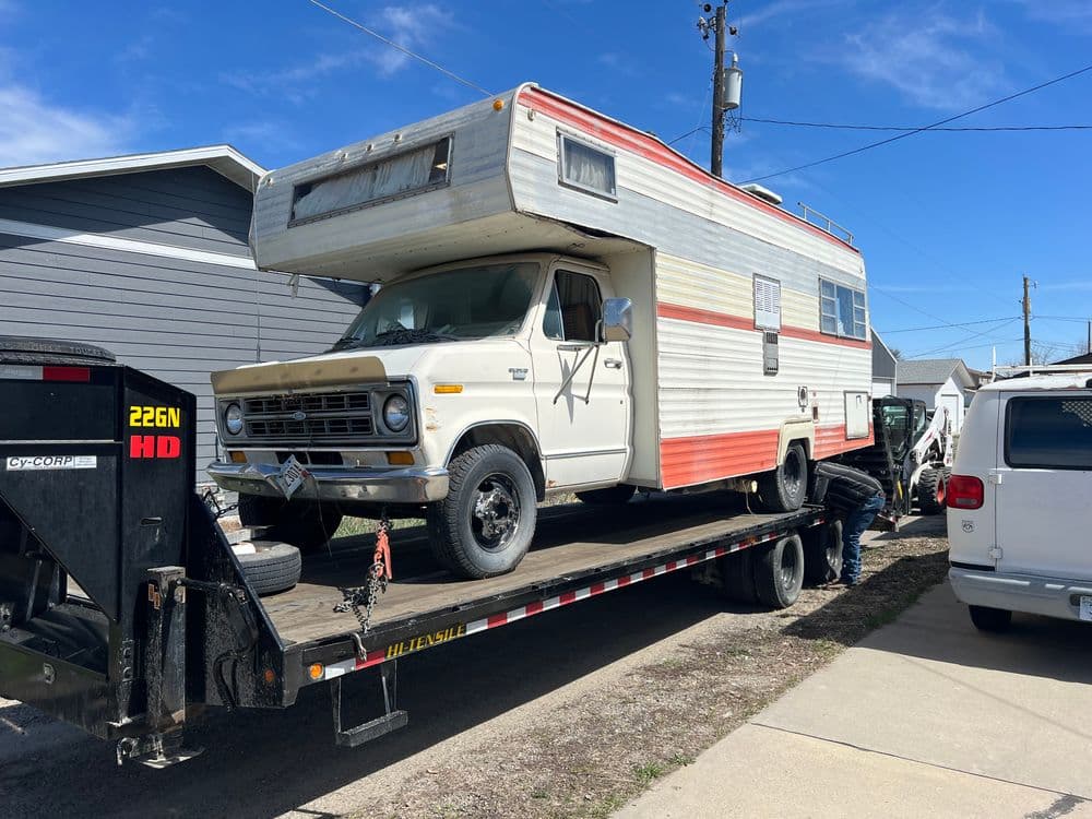 Classic vintage RV being loaded onto a tow truck in a residential area.