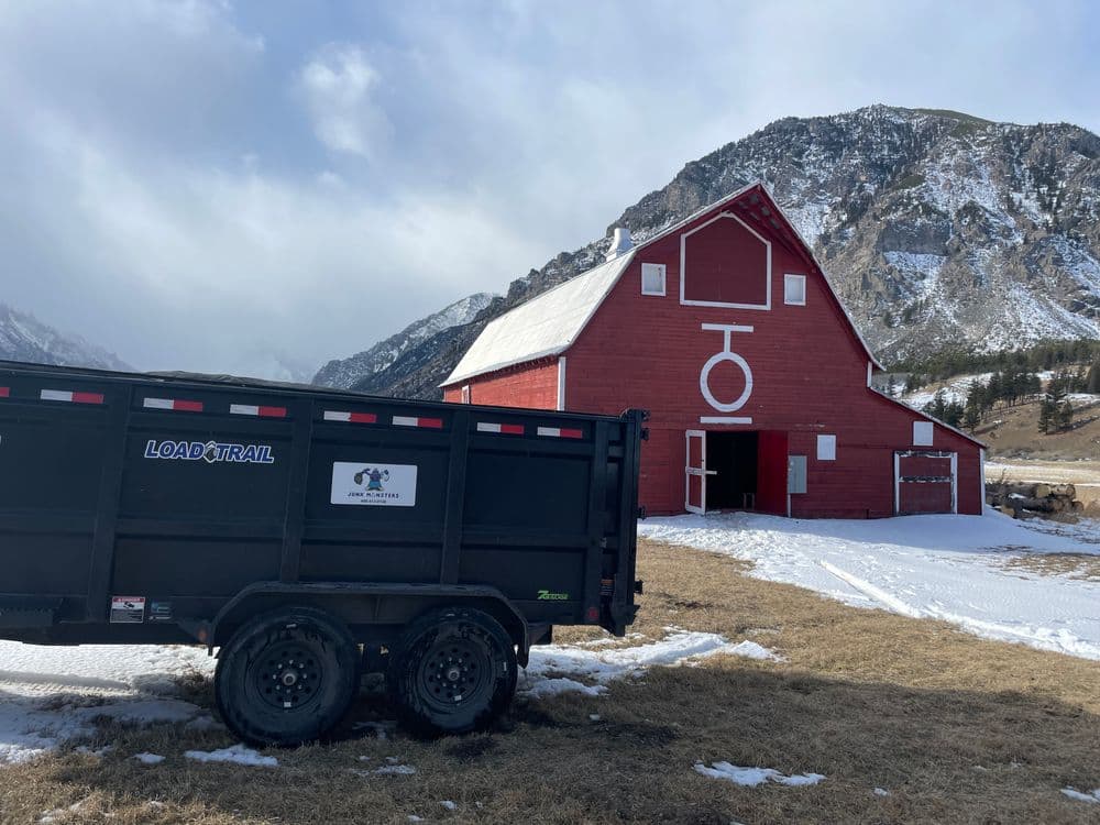 Black Load Trail trailer parked near a red barn with snow-capped mountains in the background.