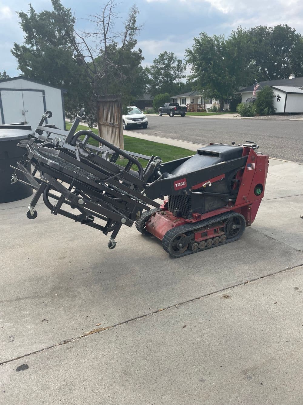 Toro lawn care machine on driveway, equipped with track system and lifting mechanism.